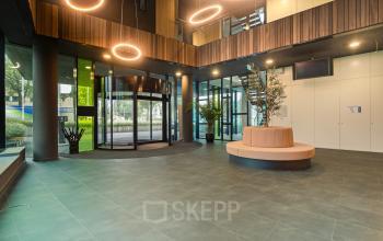 Moderne ontvangsthal in kantoorpand op Zwartewaterallee 56, Zwolle. Ruime entree met glazen wanden, draaideur en stijlvolle verlichting. Perfecte locatie voor kantoorruimte huren.