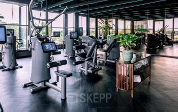 Moderne fitnessruimte in kantoorpand op Ceintuurbaan 28, Zwolle, met diverse sportapparatuur en een spiegelwand. Ideaal voor ontspanning tijdens het werken. Kantoorruimte huren met faciliteiten.