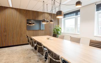 Een moderne vergaderruimte in het kantoorpand op Zuiderzeelaan 15-25, Zwolle, met een grote houten tafel, comfortabele stoelen en stijlvolle verlichting. Ideale kantoorruimte huren voor zakelijke bijeenkomsten.
