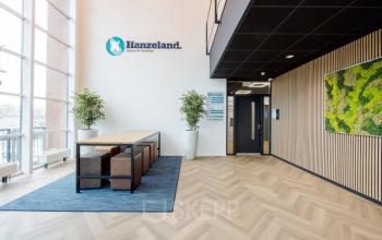 Entree van het kantoorpand op Zuiderzeelaan 15-25 in Zwolle, met moderne houten vloer en lange tafel met banken. Kantoorruimte huren in een lichte, uitnodigende omgeving.